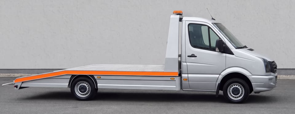 Srebrni šlep Deki Cars iz profila: visoka kabina, prazna aluminijumska platforma sa narandžastom trakom i narandžasta svetlosna rampa na uzglavlju.