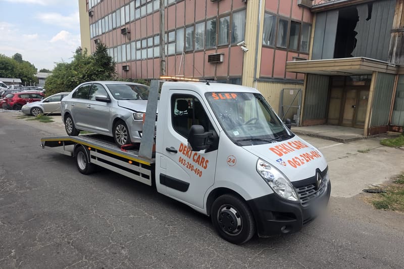 Šlep Deki Cars sa srebrnim automobilom na platformi ispred zgrade
