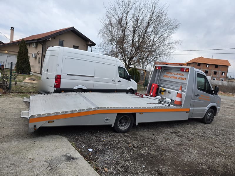 Spuštena platforma srebrnog šlepa pored belog kombija